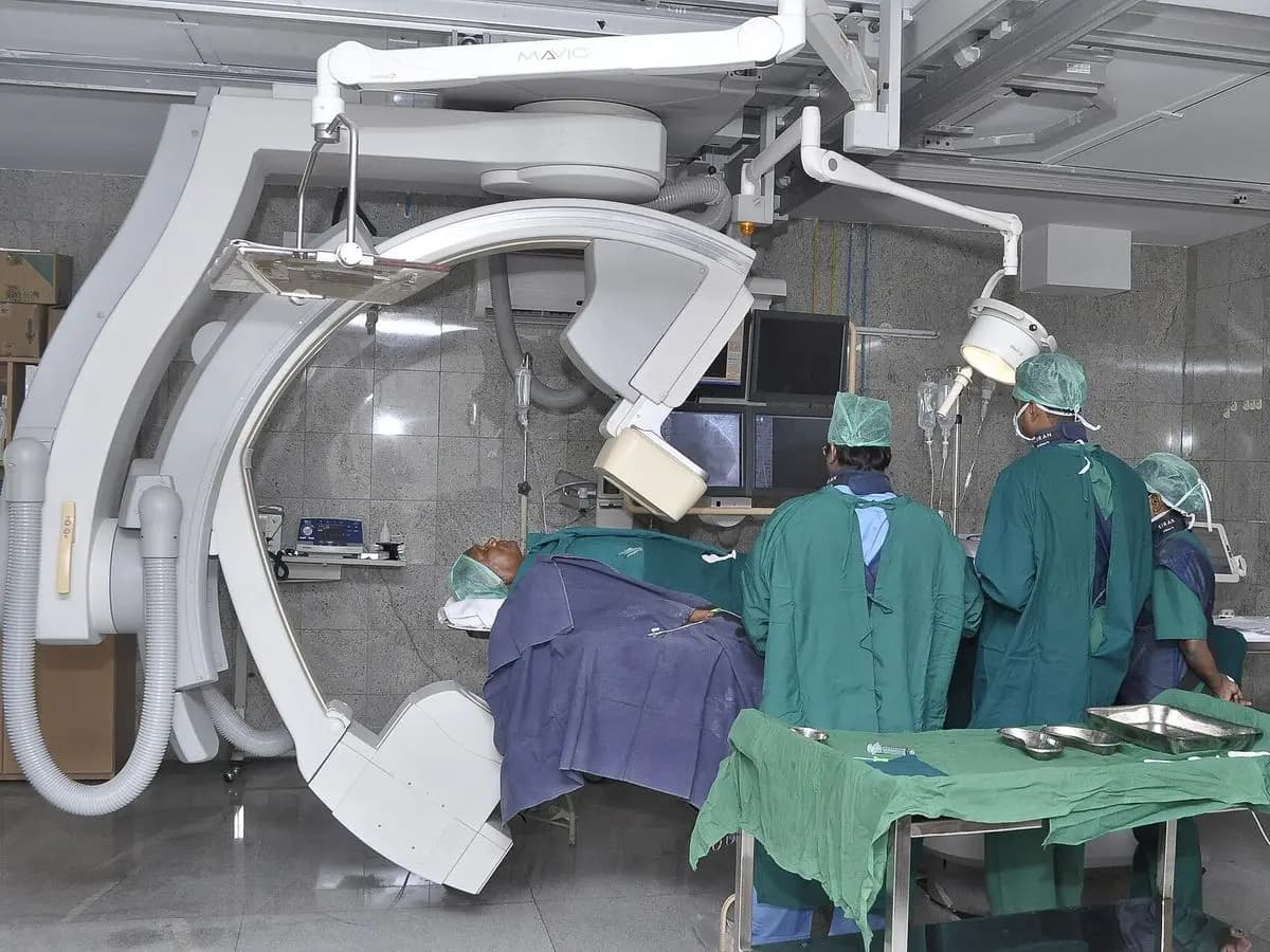 Salle de cathétérisme cardiaque : arceau d'angiographie et équipe autour de la table