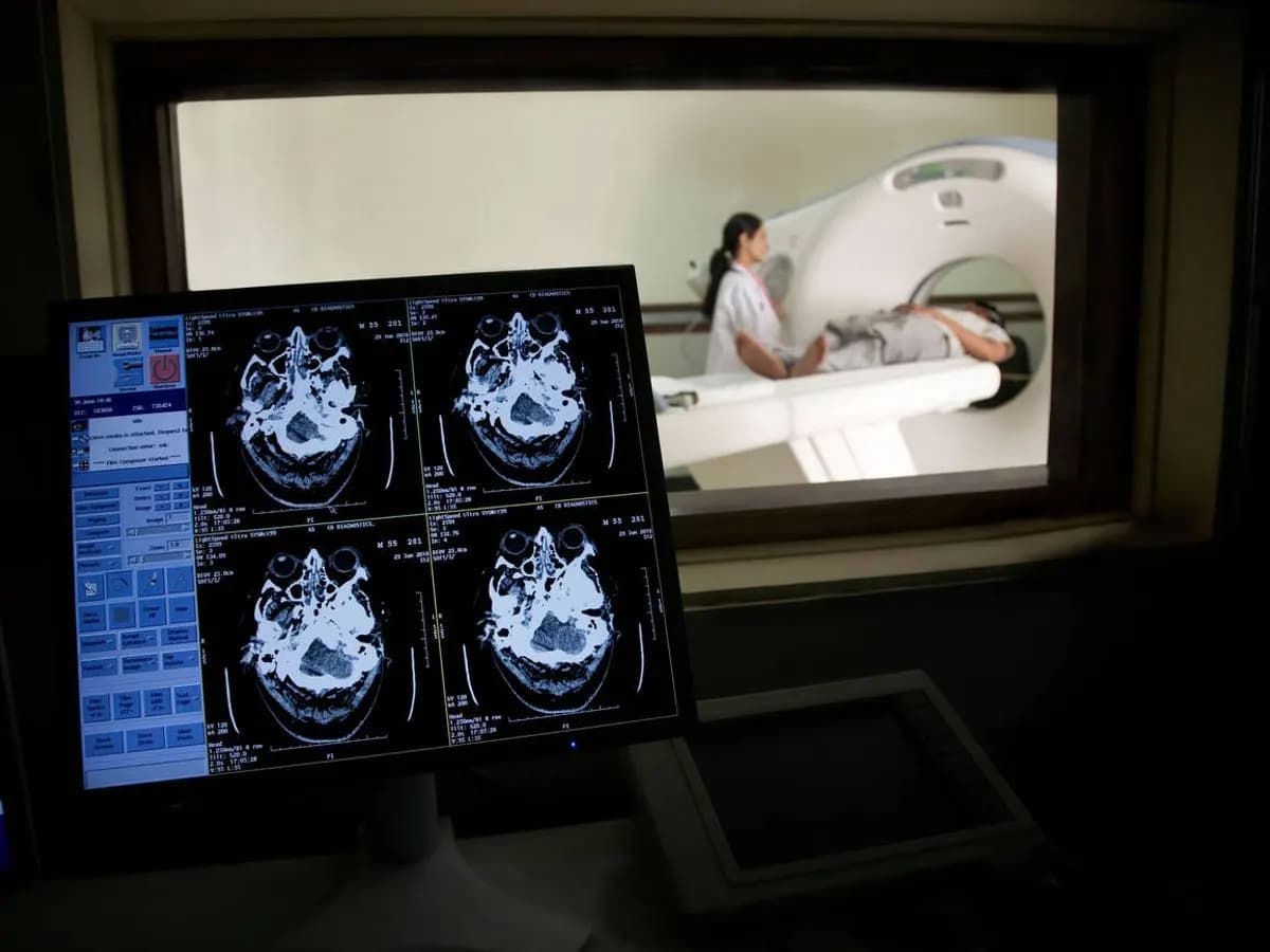 Console de scanner : coupes cérébrales à l'écran, patient dans l'anneau derrière la vitre